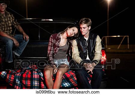 Couple sitting on tailgate of car at night View Large Photo Image Stock Photograph - Couple sitting on tailgate of car at night. Fotosearch