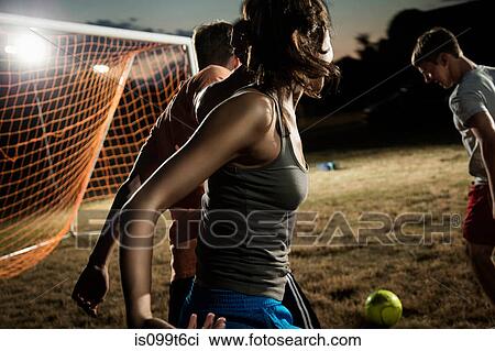 Stock Image - Friends playing soccer at night. Fotosearch