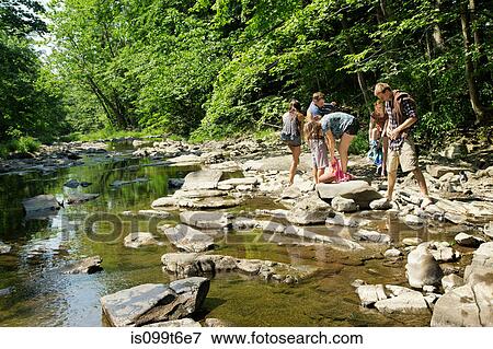 Stock Photo - Friends standing on rocks by river. Fotosearch