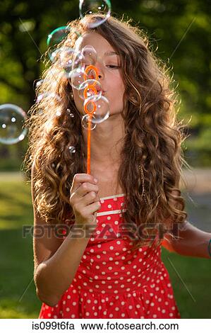 Stock Image - Girl blowing bubbles with bubble wand. Fotosearch