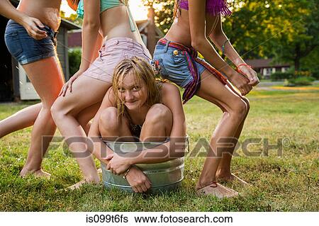 Stock Photograph - Girl crouching in bucket with friends sitting on her. Fotosearch