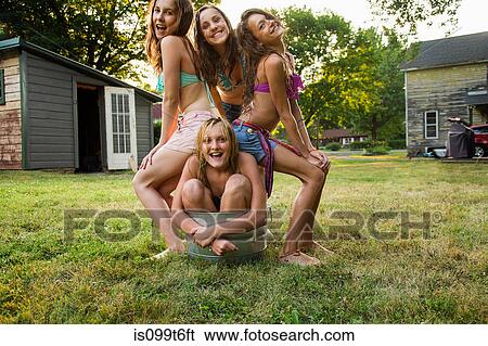 Stock Photograph - Girl crouching in bucket with friends sitting on her. Fotosearch