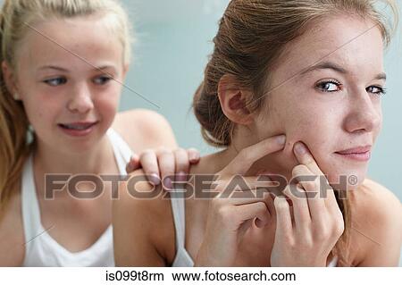 Picture - Girl squeezing a spot, friend with hand on shoulder. Fotosearch