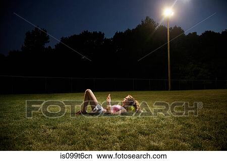 Girl using cell phone lying on soccer pitch at night View Large Photo Image Picture - Girl using cell phone lying on soccer pitch at night. Fotosearch