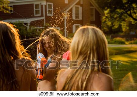 Stock Image - Girls having water fight with water pistols. Fotosearch