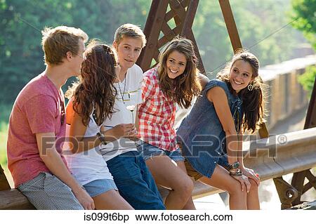 Stock Photography - Group of friends sitting on bridge. Fotosearch