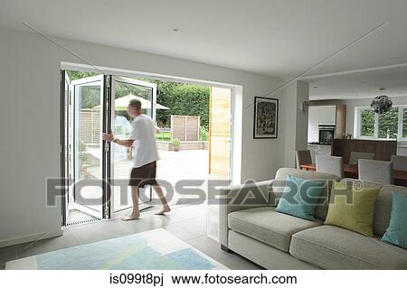 Stock Image - Man opening patio doors in living area. Fotosearch