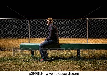 Picture - Pensive young man sitting on bleachers at night. Fotosearch