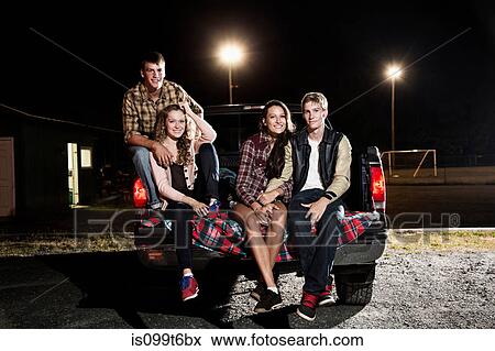 Stock Photo - Portrait of friends sitting on tailgate of car at night. Fotosearch