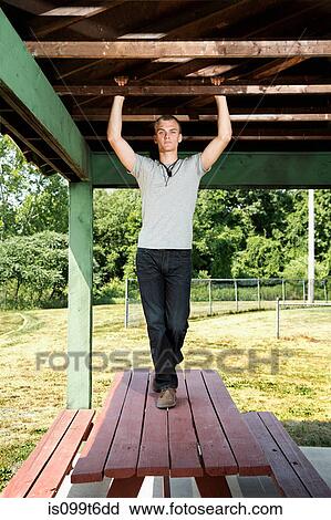 Stock Image - Portrait of young man standing on picnic table. Fotosearch