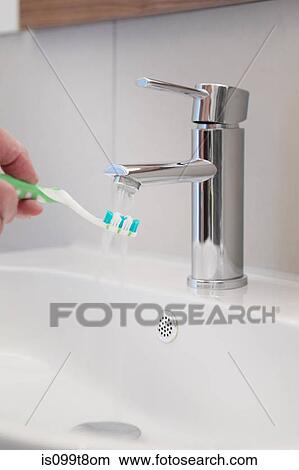Running water onto toothbrush in bathroom sink View Large Photo Image Picture - Running water onto toothbrush in bathroom sink. Fotosearch
