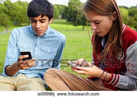 Stock Image - Teenage boy and girl using smartphones. Fotosearch