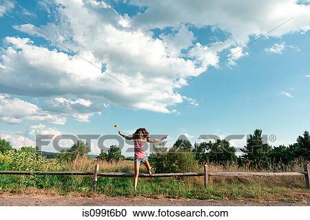 Stock Image - Teenage girl jumping off wooden fence. Fotosearch
