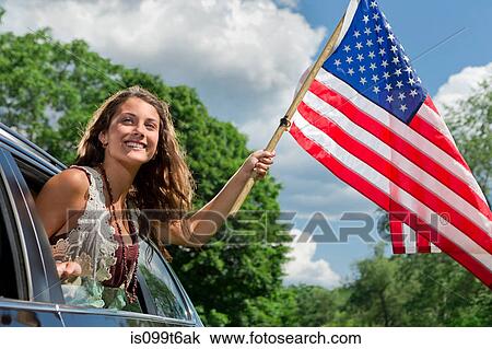 Stock Image - Teenage girl leaning out of car window holding american flag. Fotosearch