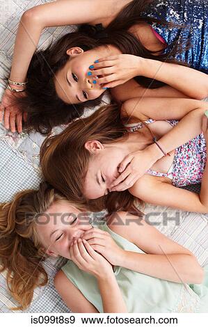 Stock Photo - Teenage girls lying on bed and giggling. Fotosearch