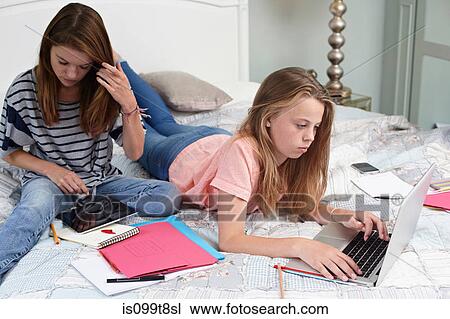 Stock Image - Teenage girls using laptop and digital tablet on bed. Fotosearch
