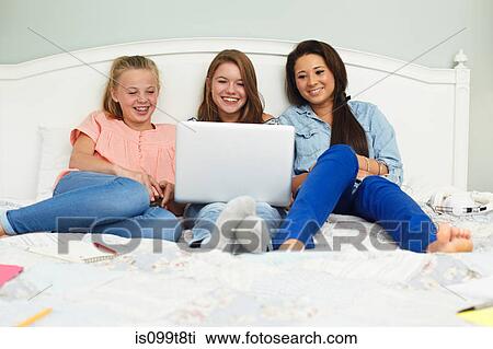 Teenage girls using laptop on bed View Large Photo Image Stock Image - Teenage girls using laptop on bed. Fotosearch