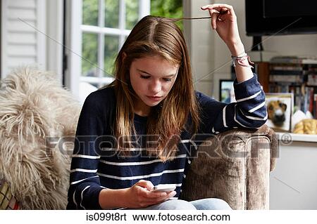 Stock Photograph - Teenage looking at cellphone and playing with her hair. Fotosearch