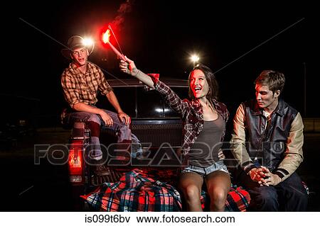 Three friends sitting on tailgate of car at night, girl holding sparkler View Large Photo Image Stock Photo - Three friends sitting on tailgate of car at night, girl holding sparkler. Fotosearch