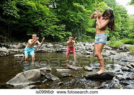 Stock Photography - Two young men splashing female friend in river. Fotosearch