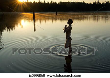 Stock Photograph - Woman meditating in calm lake. Fotosearch