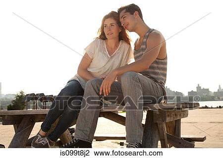 Stock Image - Young couple sitting on picnic table. Fotosearch