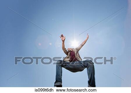 Stock Image - Young man jumping against blue sky, low angle. Fotosearch