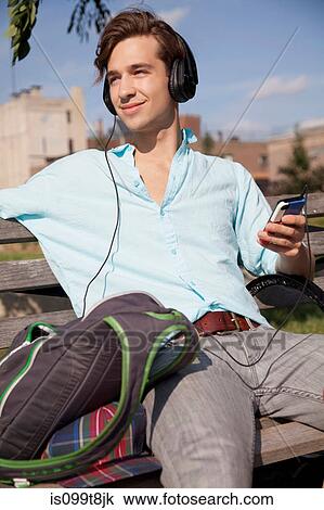 Young man sitting on bench listening to music View Large Photo Image Stock Image - Young man sitting on bench listening to music. Fotosearch