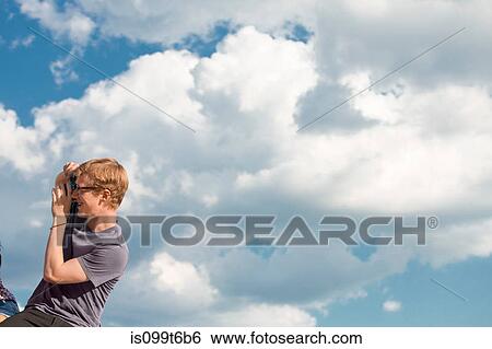 Young man taking photograph with clouds in sky View Large Photo Image Stock Photograph - Young man taking photograph with clouds in sky. Fotosearch