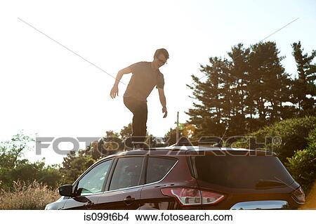 Picture - Young man walking across car roof. Fotosearch