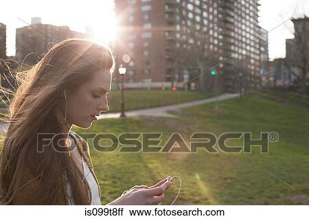 Stock Image - Young woman listening to music in park. Fotosearch