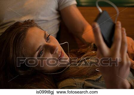 Stock Image - Young woman listening to music, lying on boyfriend's lap. Fotosearch