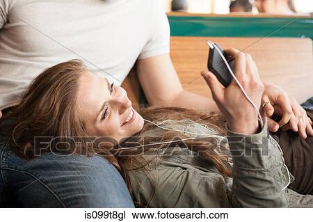 Stock Image - Young woman listening to music, lying on boyfriend's lap. Fotosearch
