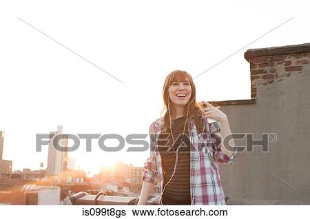 Young woman listening to music on city rooftop View Large Photo Image Stock Photograph - Young woman listening to music on city rooftop. Fotosearch