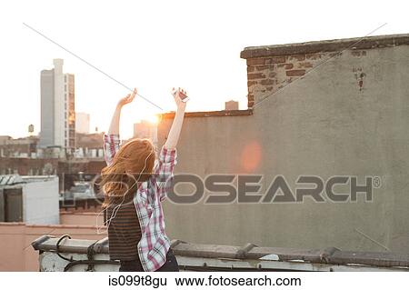 Young woman listening to music with arms raised on city rooftop View Large Photo Image Stock Photograph - Young woman listening to music with arms raised on city rooftop. Fotosearch