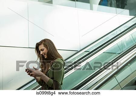 Young woman on escalator using smartphone View Large Photo Image Picture - Young woman on escalator using smartphone. Fotosearch