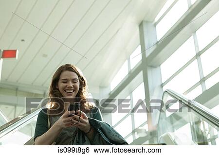 Young woman on escalator using smartphone View Large Photo Image Stock Photograph - Young woman on escalator using smartphone. Fotosearch