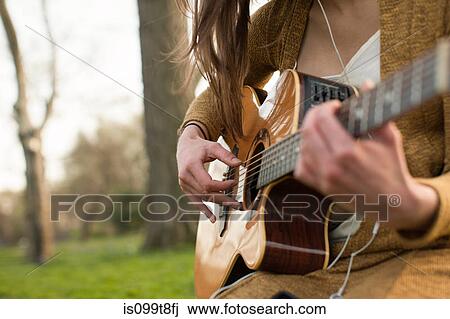 Stock Image - Young woman playing guitar outdoors. Fotosearch