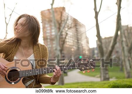 Stock Image - Young woman playing guitar outdoors. Fotosearch