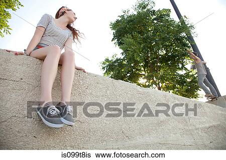 Young woman sitting on wall watching skateboarder View Large Photo Image Stock Photograph - Young woman sitting on wall watching skateboarder. Fotosearch