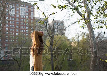 Stock Image - Young woman standing in the park. Fotosearch