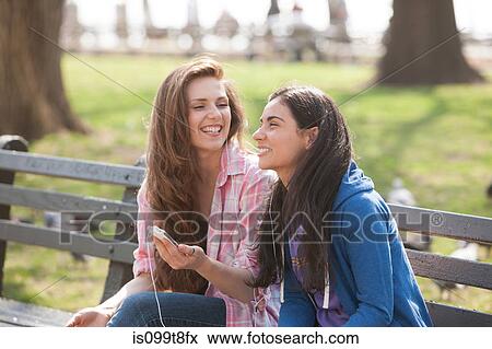 Young women sharing music in the park View Large Photo Image Stock Photo - Young women sharing music in the park. Fotosearch