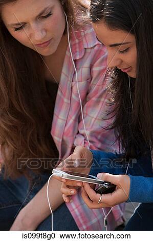 Stock Image - Young women sharing music. Fotosearch