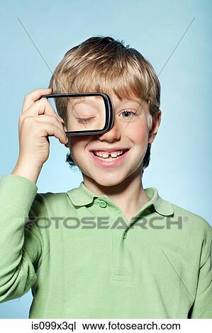 Stock Image - Boy holding smartphone over eye. Fotosearch