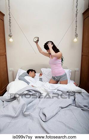 Couple in bed, woman holding alarm clock View Large Photo Image Stock Photo - Couple in bed, woman holding alarm clock. Fotosearch