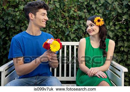 Stock Image - Couple on bench, man holding flowers. Fotosearch