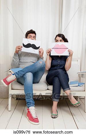 Couple sitting on sofa holding lips and moustache View Large Photo Image Stock Image - Couple sitting on sofa holding lips and moustache. Fotosearch