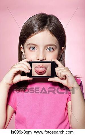 Girl holding smartphone over mouth, sticking out tongue View Large Photo Image Picture - Girl holding smartphone over mouth, sticking out tongue. Fotosearch
