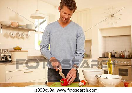 Stock Image - Man chopping red pepper in kitchen. Fotosearch