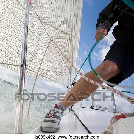 Stock Image - Man on yacht, pulling ropes. Fotosearch